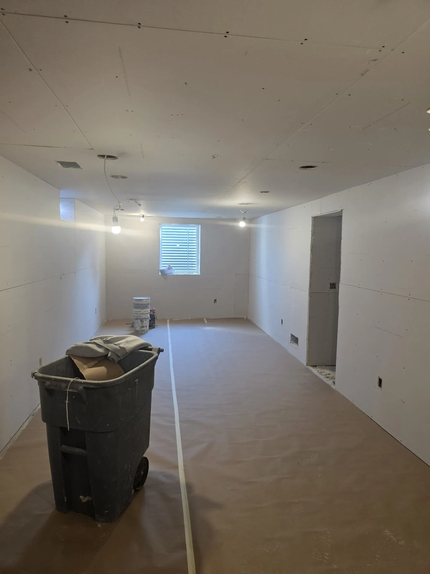 Same basement room with central window after installation of wall and ceiling drywall
