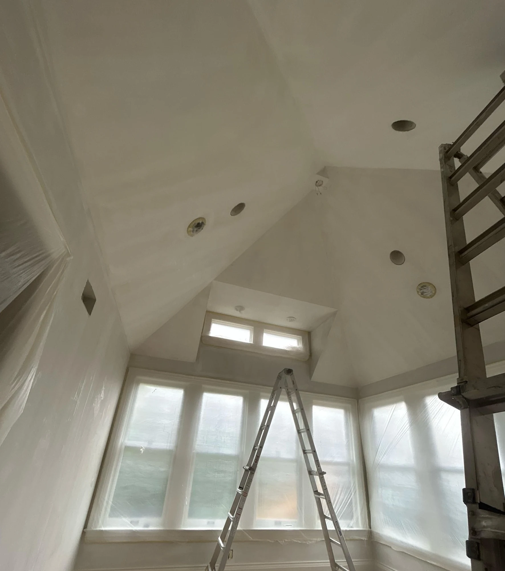 High-ceiling interior with taped and prepared walls and ladders on the jobsite