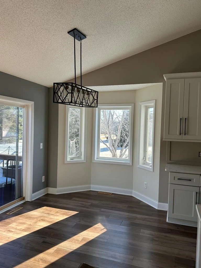 Refreshed dining nook with light gray walls, white cabinets, dark wood flooring and black pendant light