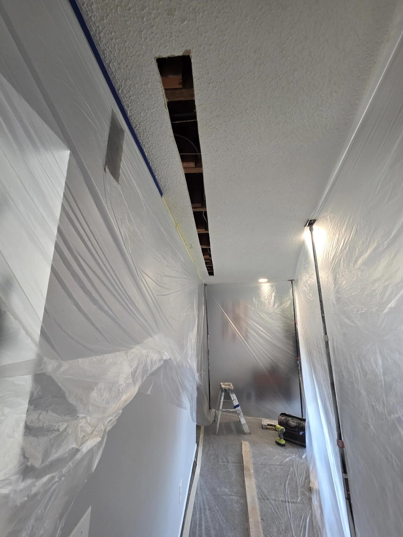 Narrow ceiling opening along protected hallway with exposed framing and wiring