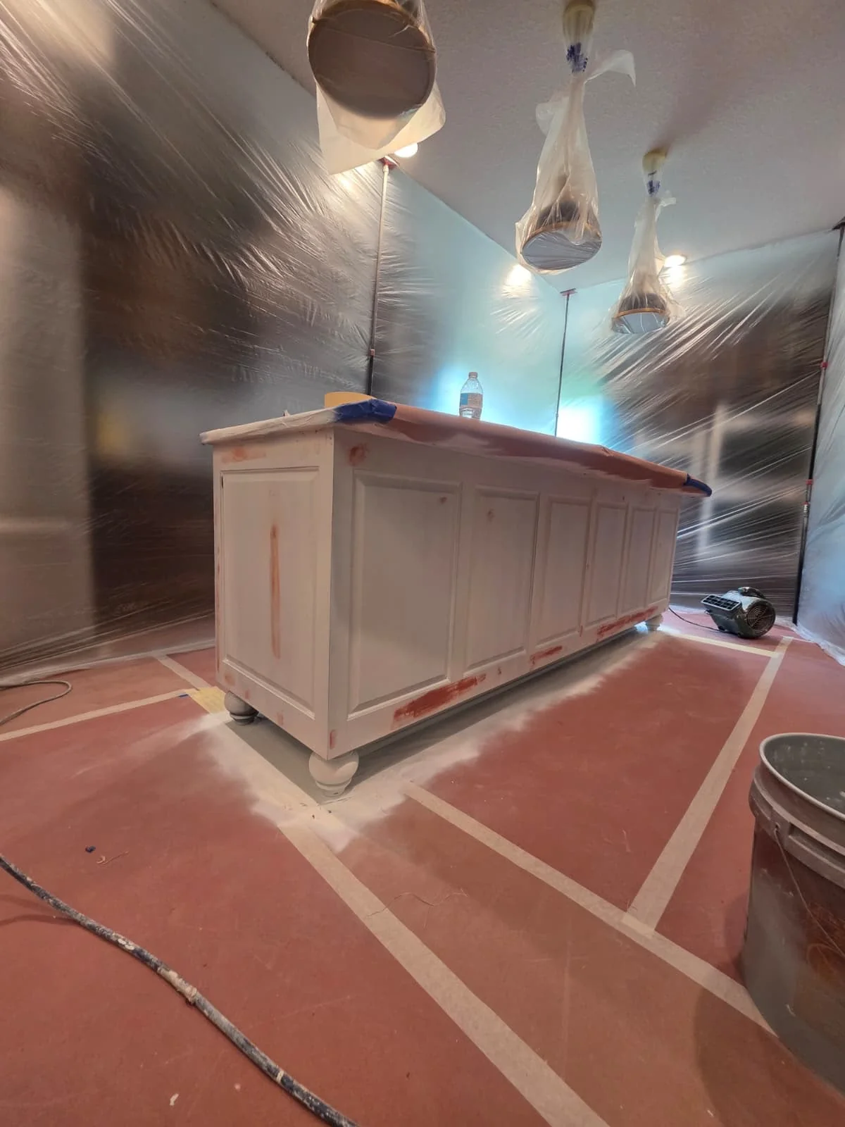 Kitchen island with light primer and visible touch-up areas in a protected spray workspace