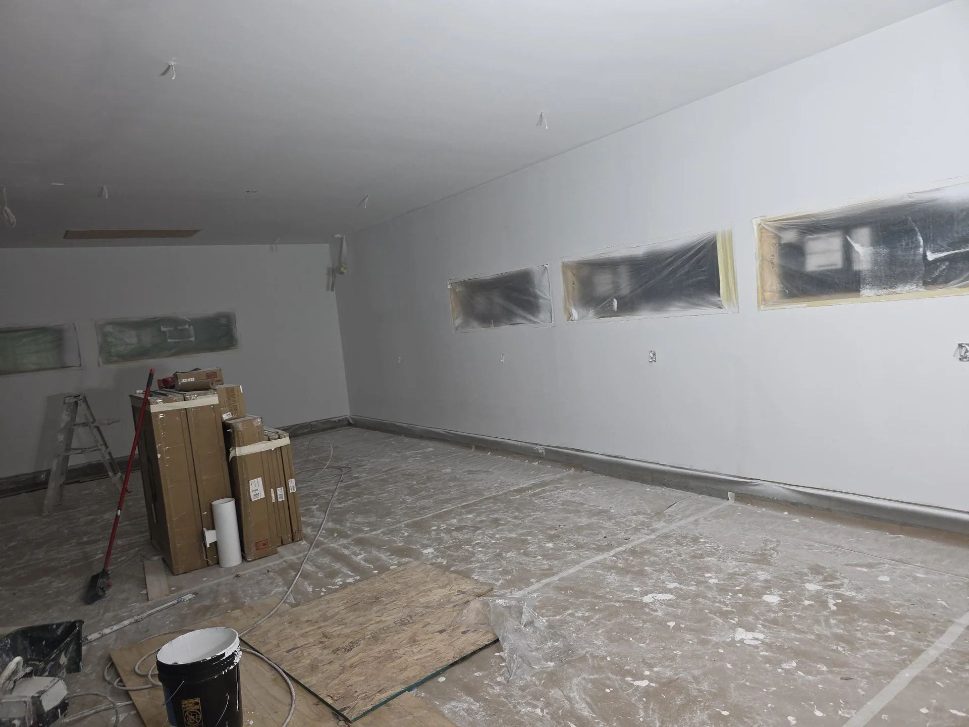 Large room with smooth light-colored walls and narrow windows masked for ongoing finishing work