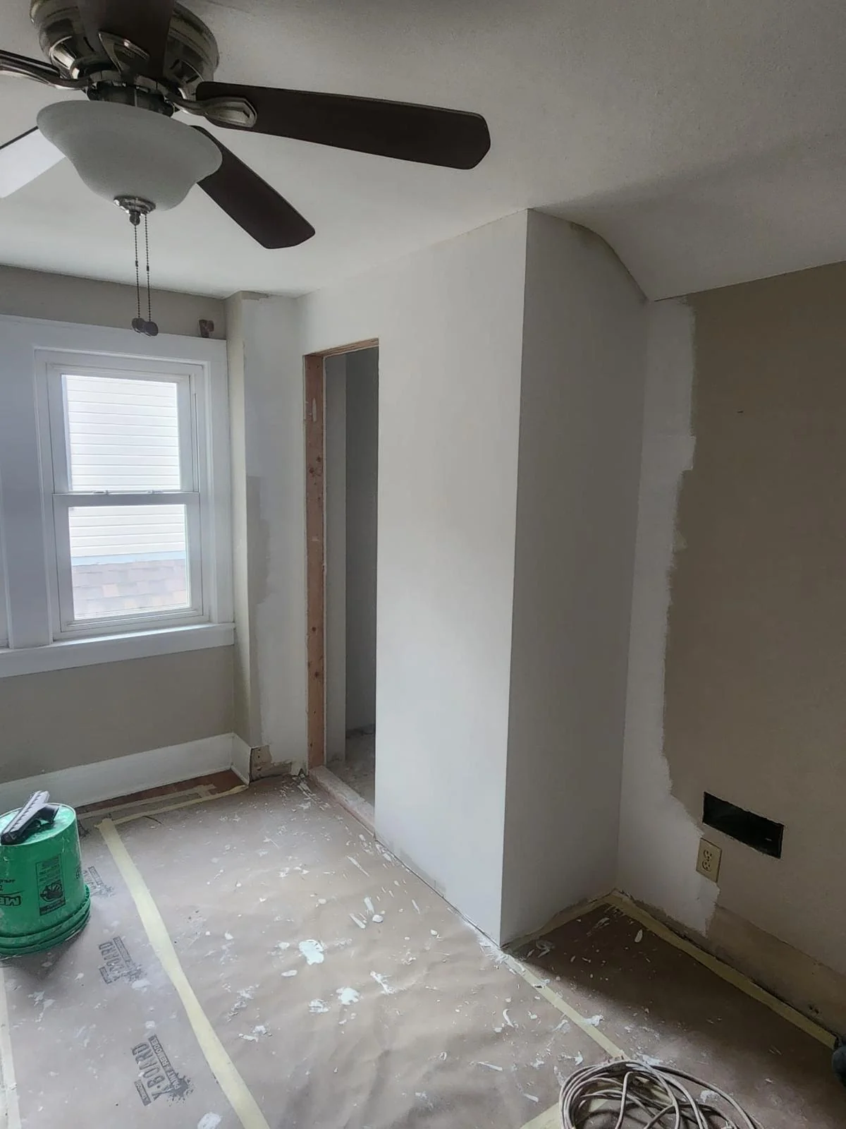 Same interior corner after drywall panels and joint compound, with window and ceiling fan visible