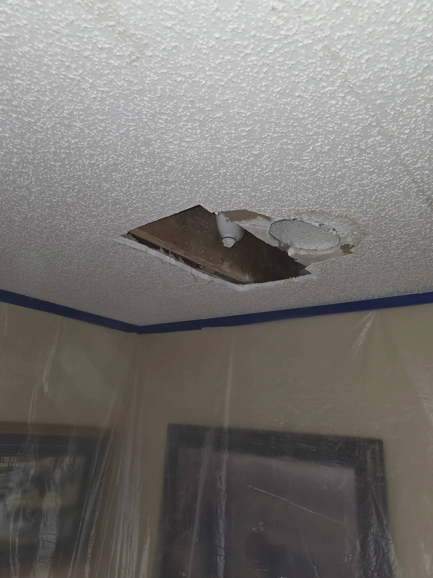 Textured ceiling with open damaged patch and protected furnishings